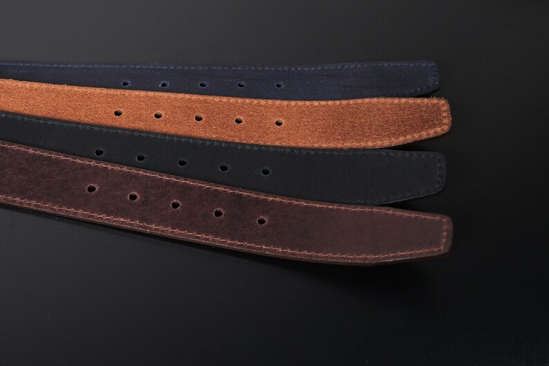 May include: A set of four belts in navy blue, tan, black, and dark brown. Each belt features a textured suede-like finish, visible stitching along the edges, and a series of evenly spaced circular adjustment holes running along the length of the strap.