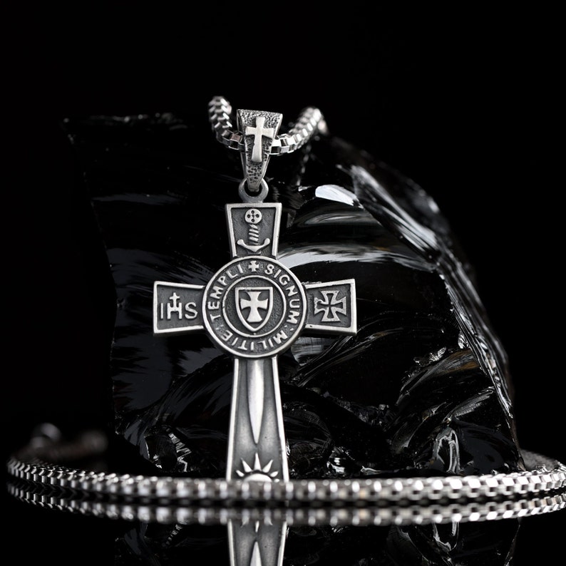May include: Silver pendant necklace with a cross design. The cross features a sword, a shield, and the words "TEMPLI MILITIE SIGNUM" and "IHS".