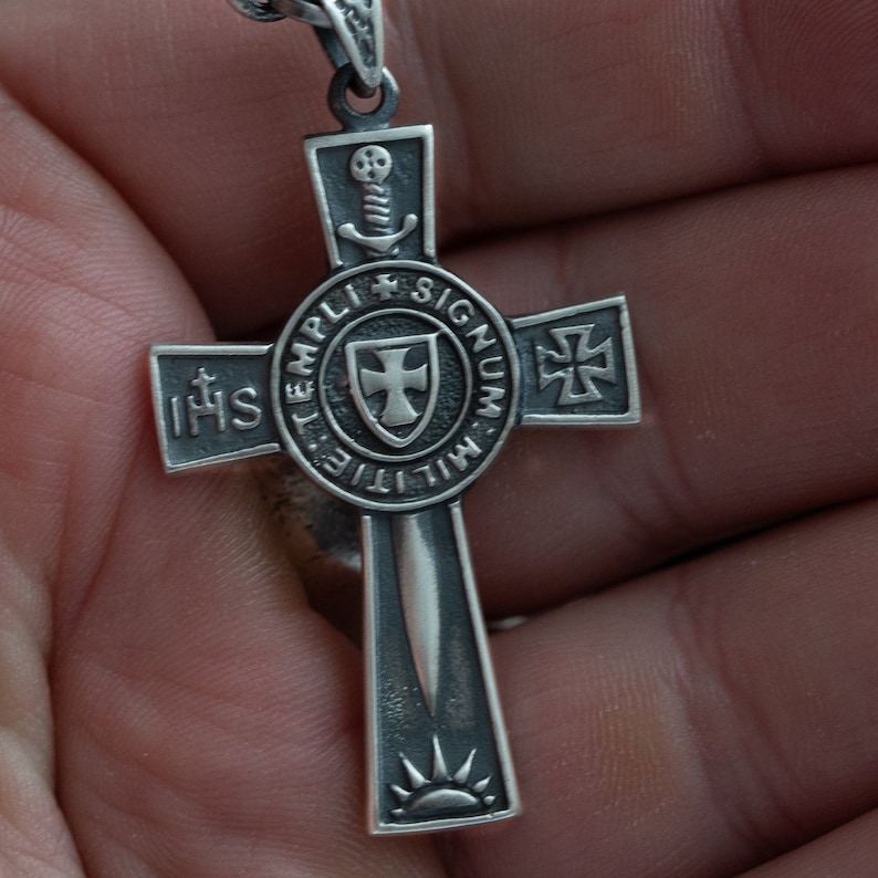 May include: Silver cross pendant with a sword, shield, and the text "MILITIE TEMPLI SIGNUM" around the shield. The cross also has the text "IHS" on one arm and a swastika on another arm.