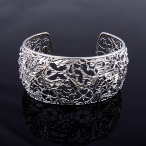 May include: A silver filigree cuff bracelet with a floral design. The bracelet is open on one side and has a delicate, intricate pattern.