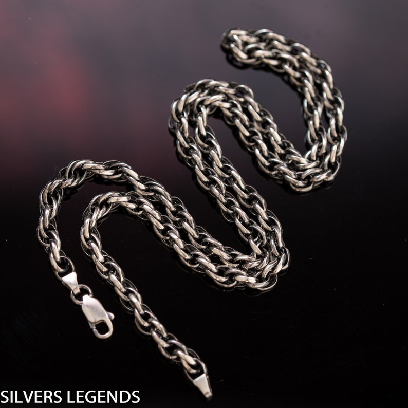 May include: A silver chain necklace with a twisted rope design. The chain is laid out in a figure eight shape on a black surface.
