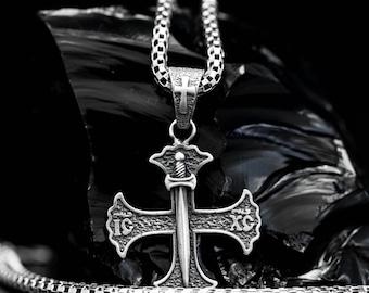 May include: A silver chain necklace with a pendant featuring a cross with a sword in the center. The cross has the letters "IC" and "XC" on the top and bottom arms. The pendant is on a black background.