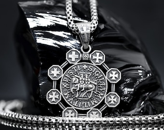May include: A silver necklace with a pendant featuring a circular design with the words "XPISTI SIGILLVM MILITVM" and a depiction of a knight riding a horse. The pendant is surrounded by eight smaller crosses.