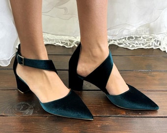 May include: A pair of dark green velvet heeled shoes with ankle straps. The shoes have a pointed toe and a block heel.