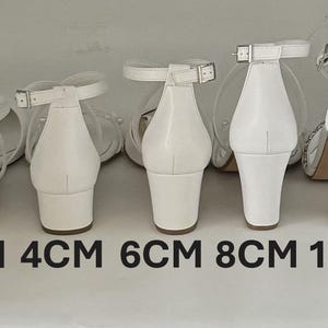以下が含まれることがあります： 2cm、4cm、6cm、8cm、10cmと表示された、異なるヒール高さの白いヒールサンダルが5足あります。