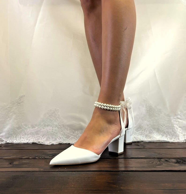 May include: White bridal shoes with a pearl ankle strap and a block heel.