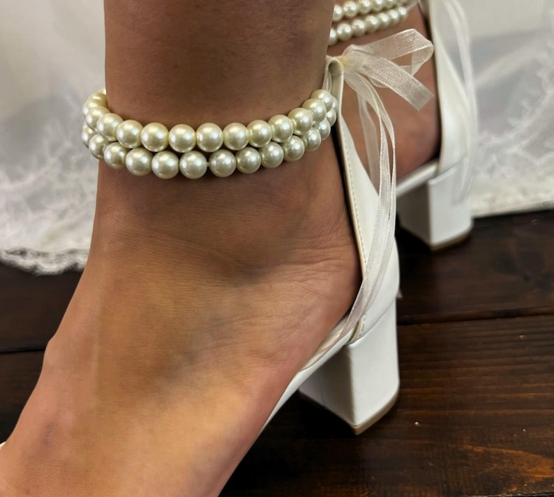 May include: White bridal ankle bracelet with a double row of faux pearls and a white satin ribbon.