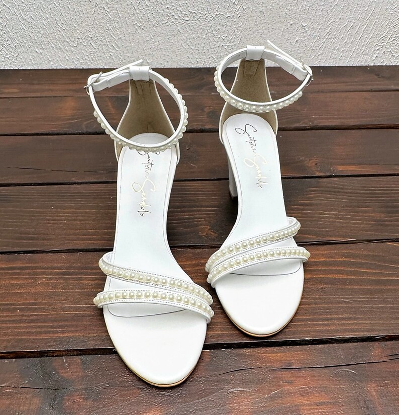 Puede incluir: Sandalias blancas de tac&oacute;n con adornos de perlas y tiras de tobillo. Las sandalias tienen el texto "Something Special" escrito en el interior de las tiras.