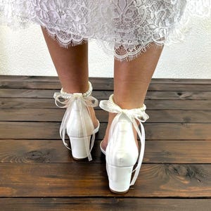 May include: White satin heeled sandals with a pearl ankle strap and a white satin bow. The sandals have a block heel.
