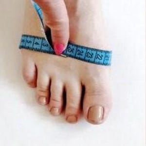 May include: Close-up of a foot with a blue measuring tape wrapped around the ankle. The tape reads 22 inches.