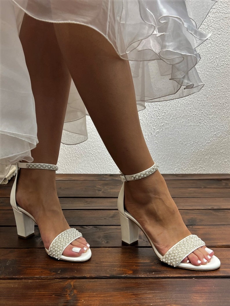 Puede incluir: Sandalias blancas de sat&eacute;n con tac&oacute;n y adorno de perlas en la tira del tobillo y la tira del dedo del pie. Los tacones son tacones de bloque.