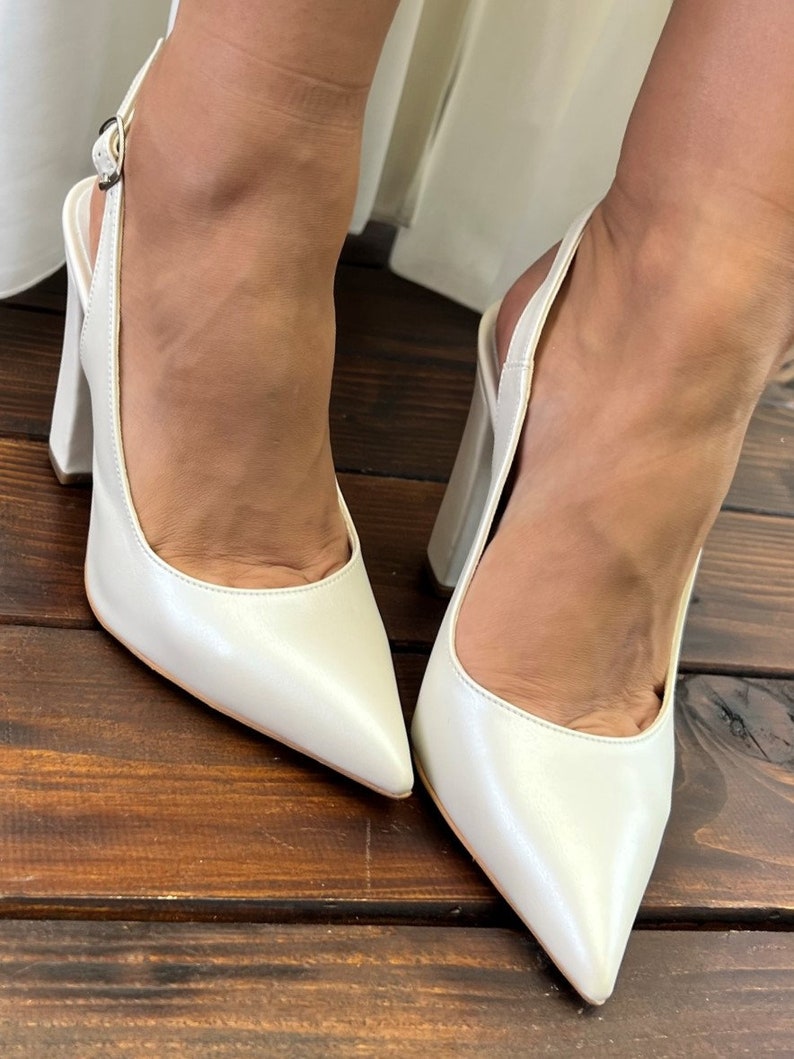 May include: A pair of white leather slingback heels with a pointed toe and a block heel.