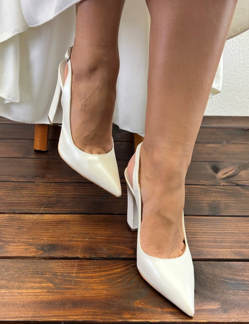 May include: A pair of white leather slingback heels with a pointed toe and a block heel.