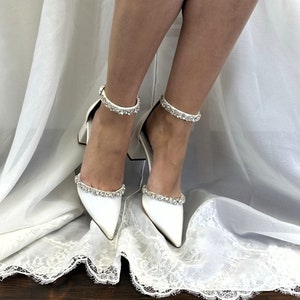 May include: White satin bridal heels with a pointed toe and ankle strap adorned with crystal embellishments.