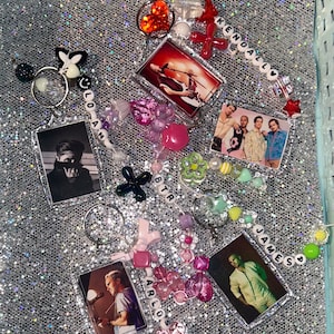 May include: A collection of keychains featuring different band members. Each keychain has a clear plastic frame with a photo of a band member and a beaded charm with their name. The charms are made with colorful beads, including pink, green, blue, and white. The names on the charms are: Kendall, Loan, BTR, Arlo, and James.