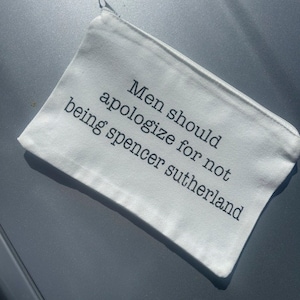 May include: White canvas zippered pouch with the text "Men should apologize for not being Spencer Sutherland" printed in black.