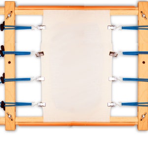 May include: A wooden embroidery hoop with a white fabric stretched across it. The hoop is held together with blue elastic straps and metal clips.