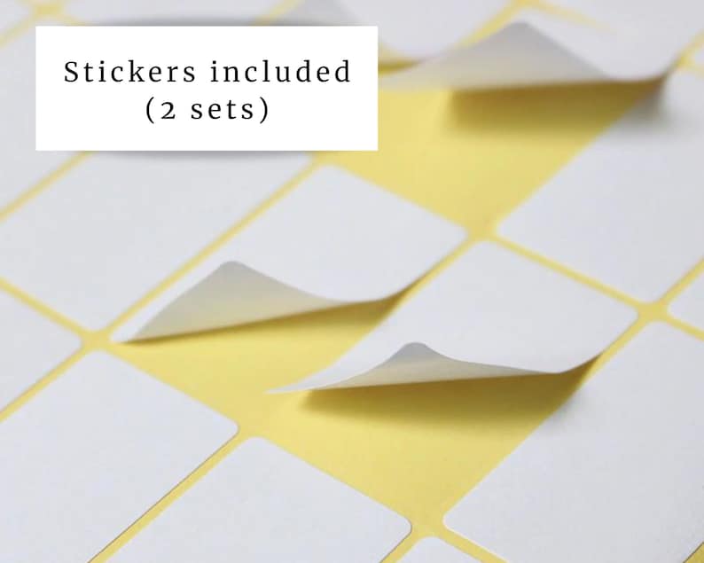 May include: Close-up of white rectangular stickers with a peel-off corner, arranged on a yellow background. The text "Stickers included (2 sets)" is in a white rectangle in the upper left corner. The stickers are arranged in a grid pattern.