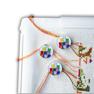 May include: White Aida cloth with colorful cat embroidery designs on three round felt pincushions. The pincushions are attached to the cloth with colorful embroidery floss.