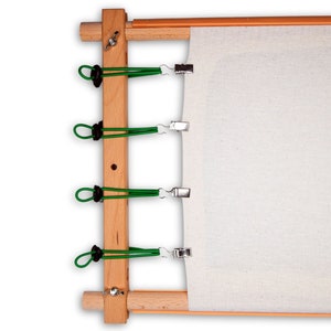 May include: A wooden embroidery hoop with a white fabric stretched across it. The fabric is secured with four green clips.