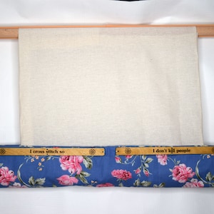 May include: Wooden embroidery frame with a canvas stretched across it. The bottom bar is covered in blue floral fabric with the text "I cross stitch so" and "I don't kill people" on wooden plaques.