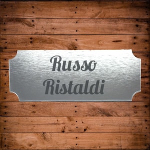 May include: A silver metal sign with the text "Russo Ristaldi" in a cursive font.