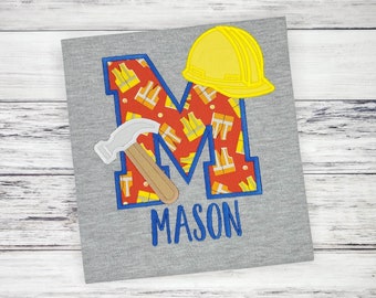 May include: A grey t-shirt with a blue and red letter M, a yellow hard hat, a hammer, and the name "MASON" in blue letters.