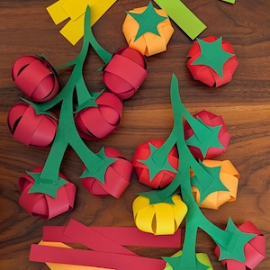 May include: Paper craft tomatoes in red, orange, and yellow, constructed from looped paper strips with green paper stems and vines. The set includes two main vine structures with attached fruit and several loose paper strips in various colours.