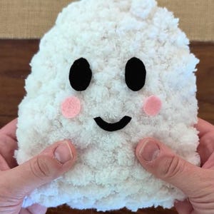 Puede incluir: Un juguete de fantasma de peluche blanco hecho de hilo suave y esponjoso. El fantasma presenta dos ojos ovalados de fieltro negro, una boca curva de fieltro negro y dos pequeñas mejillas circulares de fieltro rosa en el cuerpo blanco.