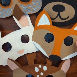 May include: A collection of five animal masks including an owl with blue and grey feathers, a black bear, a white rabbit, an orange and tan fox, and a brown deer with white spots. Each mask features circular cutouts for the eyes.