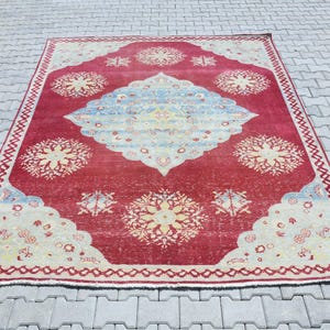 May include: A vintage red rug with a cream and blue floral pattern. The rug has a faded look and a worn border.