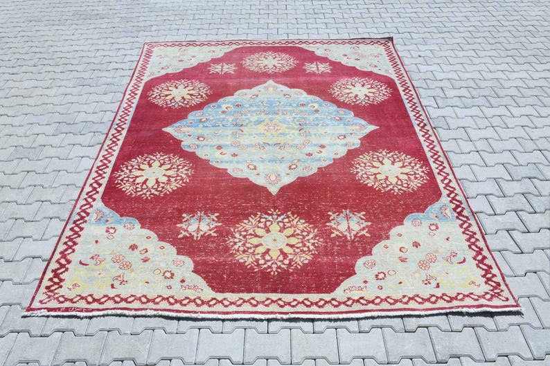 May include: A vintage red rug with a cream and blue floral pattern. The rug has a faded look and a worn border.