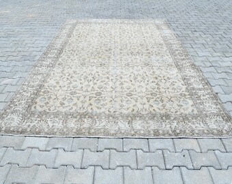 Op de afbeelding: Een rechthoekig, beige tapijt met een ingewikkeld bloemenpatroon en een donkerbruine rand. Het tapijt ligt op een grijs, getextureerd oppervlak en toont het gedetailleerde ontwerp en kleurenpalet.