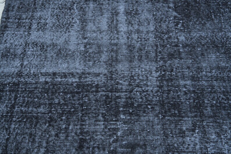 May include: A rectangular area rug featuring a distressed, weathered texture in shades of deep charcoal, slate gray, and faded black. The surface displays a dense, woven grid pattern with uneven color distribution, creating a worn, aged appearance.