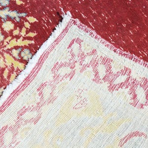 May include: Close-up of a cream-colored rug with a red border. The rug has a repeating pattern of red floral designs.