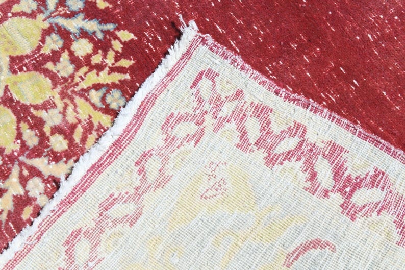 May include: Close-up of a cream-colored rug with a red border. The rug has a repeating pattern of red floral designs.