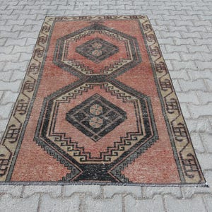 Puede incluir: Una alfombra vintage con un patrón geométrico en tonos rojos, negros y crema. La alfombra tiene un aspecto desgastado y es perfecta para añadir un toque de estilo bohemio a cualquier habitación.