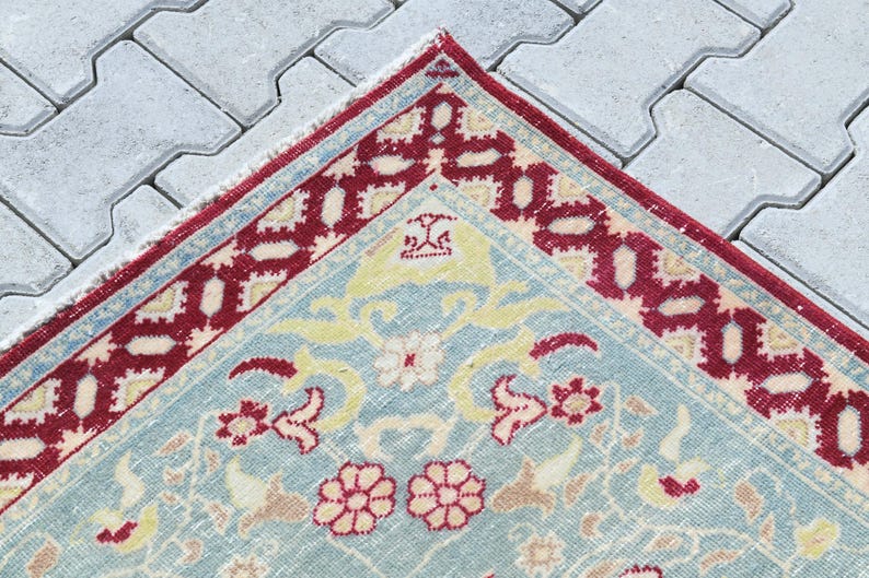 May include: A vintage rug with a light blue background and a red and white border. The rug has a floral pattern with yellow, pink, and white flowers.