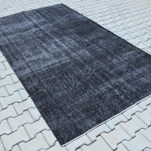 May include: A rectangular area rug featuring a distressed, faded black and dark gray color palette. The surface displays a worn, mottled texture with subtle variations in tone across the entire piece, creating a weathered appearance throughout.