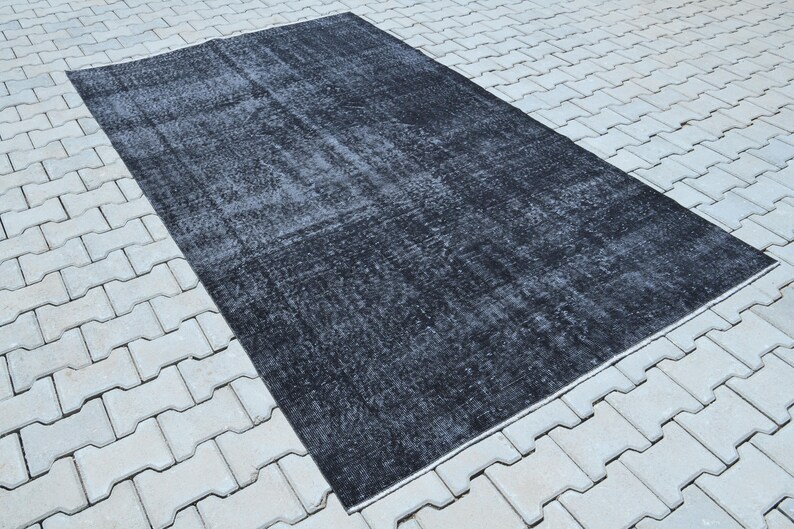 May include: A rectangular area rug featuring a distressed, faded black and dark gray color palette. The surface displays a worn, mottled texture with subtle variations in tone across the entire piece, creating a weathered appearance throughout.