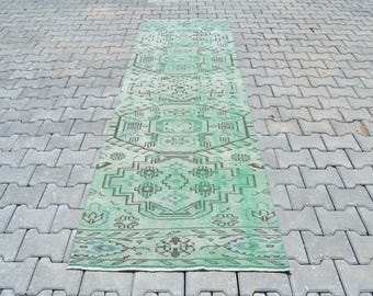 May include: A green and white vintage kilim rug with a geometric pattern. The rug is laid out on a gray concrete surface.