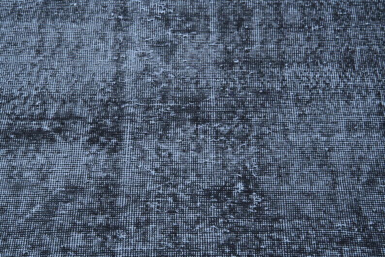 May include: A woven textile rug featuring a dense, grid-like pattern in shades of dark charcoal black and muted slate blue. The surface displays a distressed, weathered appearance with uneven color distribution across the entire fabric weave.