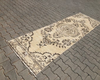 Könnte beinhalten: Ein vintage cremefarbener Teppich mit braunem Blumenmuster. Der Teppich hat einen abgenutzten Look und ist perfekt, um Ihrem Zuhause einen Hauch von Boho-Stil zu verleihen.