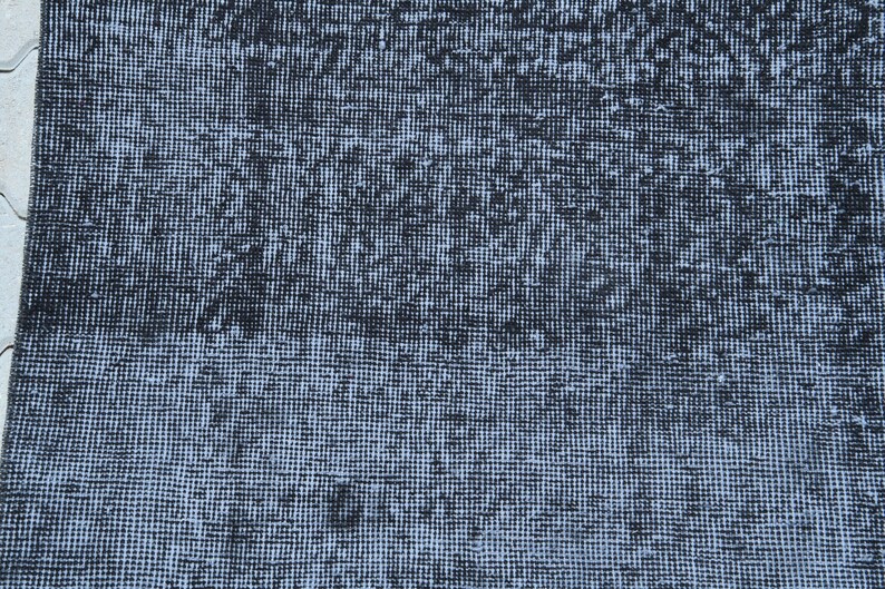 May include: A rectangular area rug featuring a dense, woven texture with a distressed aesthetic. The surface displays a mottled pattern of deep black and faded light gray tones, creating a high-contrast, weathered appearance across the entire fabric.