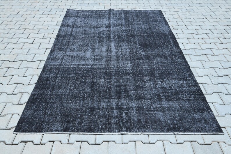 May include: A rectangular area rug featuring a distressed, faded black and dark charcoal gray color palette. The surface displays a worn, mottled texture with subtle variations in tone across the entire field, creating a weathered appearance.