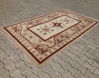 May include: A beige and red patterned rug with a geometric design. The rug has a fringe border.