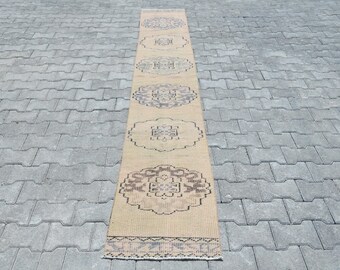 May include: A beige runner rug with a repeating pattern of brown floral designs. The rug has a fringe border.