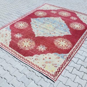May include: A vintage red rug with a cream-colored border and intricate floral patterns in shades of cream, yellow, and blue.