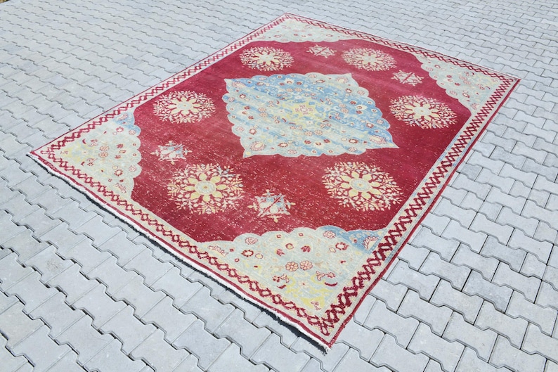 May include: A vintage red rug with a cream-colored border and intricate floral patterns in shades of cream, yellow, and blue.