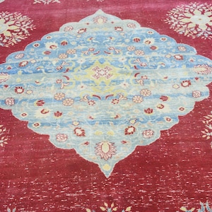 May include: A red rug with a blue and white floral pattern in the center. The rug has a distressed look and is made of wool.